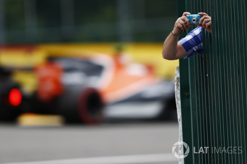 A fan leans out to take some photos as Stoffel Vandoorne, McLaren MCL32, passes through the background