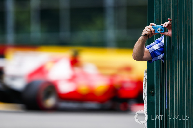 A fan leans through some bars to take a photo as Sebastian Vettel, Ferrari SF70H, passes by in the background