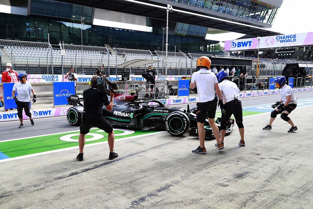 McLaren pit crew members attempt to assist Valtteri Bottas, Mercedes W12, in the pit lane