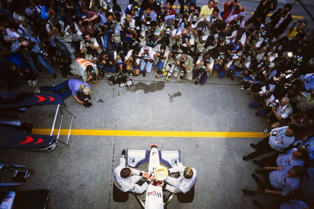 Mika Häkkinen, McLaren MP4-13 Mercedes, and David Coulthard, McLaren MP4-13 Mercedes, celebrate victory in the race and the world championship opposite a bank of photographers