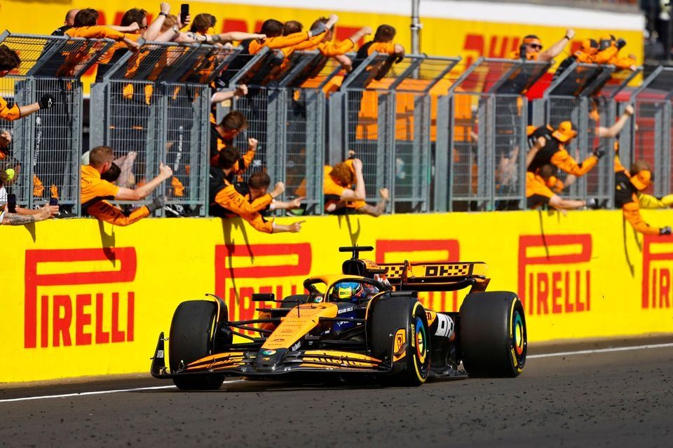 Oscar Piastri, McLaren MCL38, 1. pozycja, mija sw&oacute;j świętujący zesp&oacute;ł na pit wallu pod koniec wyścigu.