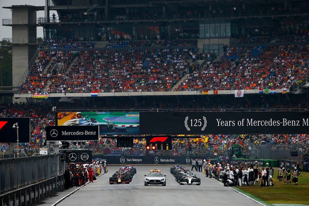 The Safety Car leads Lewis Hamilton, Mercedes AMG F1 W10, Max Verstappen, Red Bull Racing RB15, and the rest of the field away