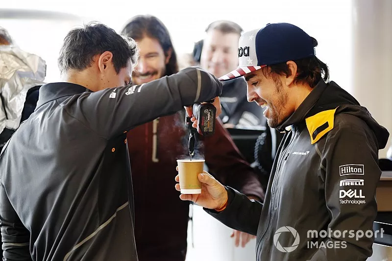 Lando Norris, McLaren, agita una taza de t&eacute; con una herramienta el&eacute;ctrica para Fernando Alonso, McLaren, mientras el conductor de IndyCar JR Hildebrand observa en el garaje