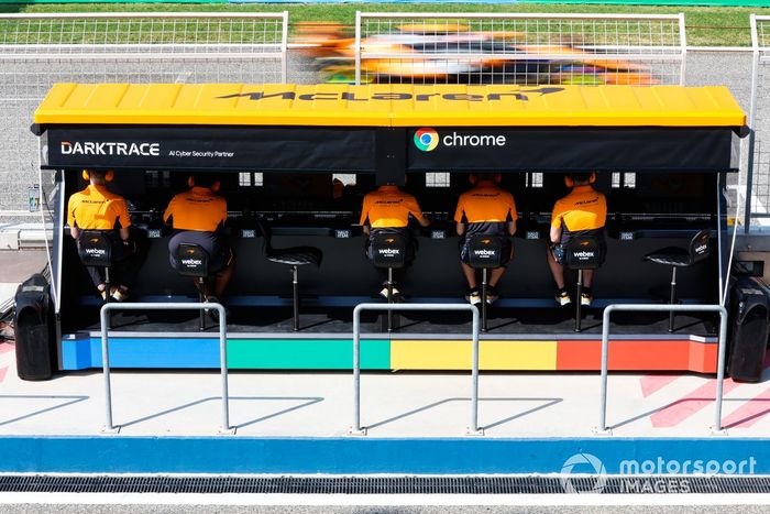 Los ingenieros del equipo McLaren F1 se sientan en el muro de boxes, mientras Lando Norris, McLaren MCL38, pasa en pista.