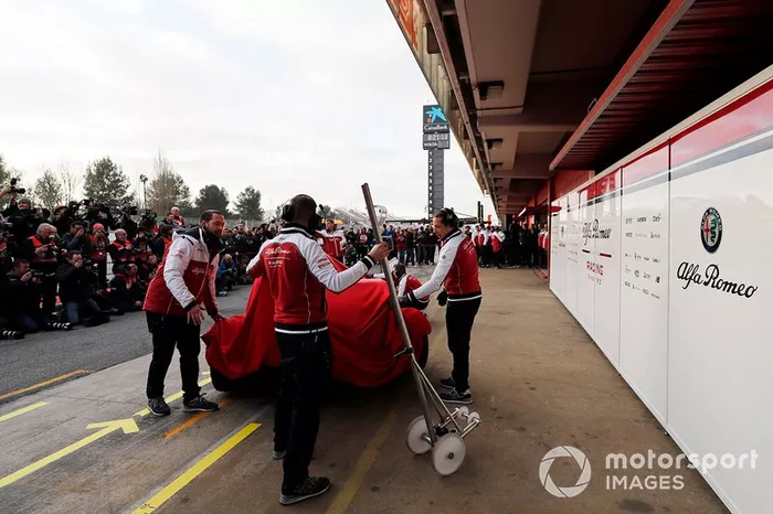 Les mécaniciens Alfa Romeo Racing avec l'Alfa Romeo Racing C38 sous un drap
