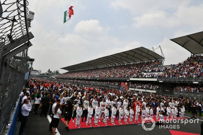 Los pilotos se paran con las mascotas de Grid Kid durante el himno nacional mientras un helicóptero ondea la bandera antes de la salida