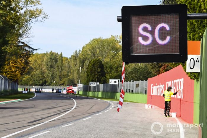 Un pintor retoca carteles de patrocinadores cerca del anuncio de Safety Car