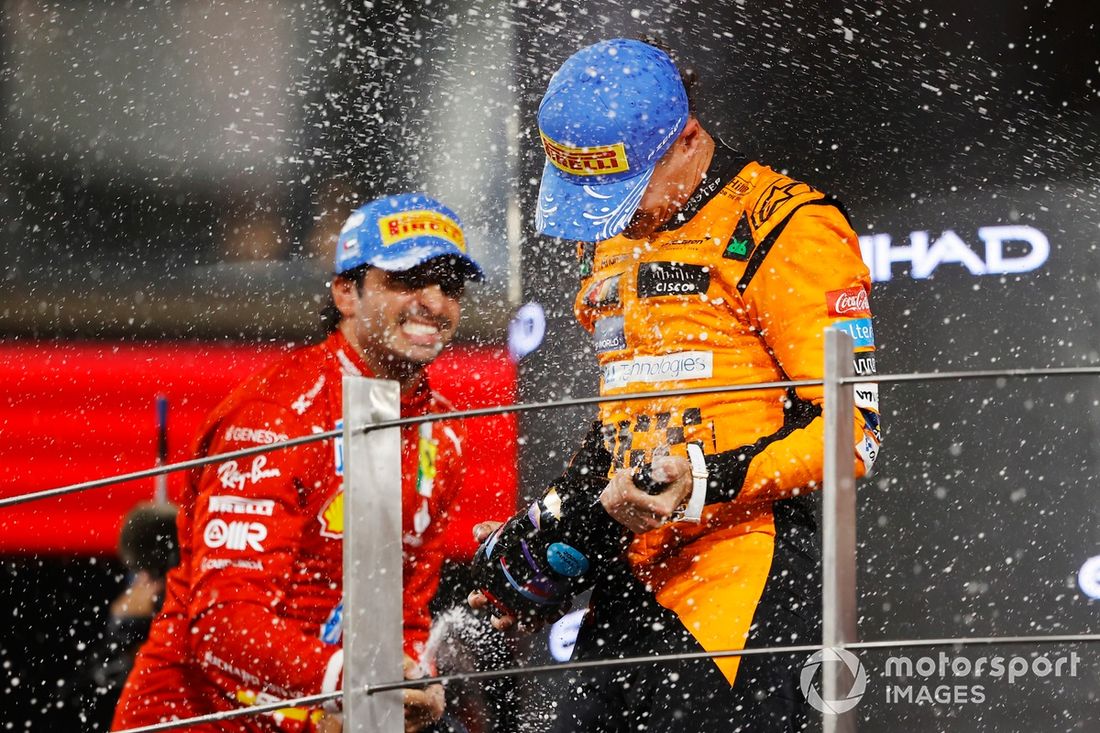 Carlos Sainz, Scuderia Ferrari, 2. miejsce, Lando Norris, McLaren F1 Team, 1. miejsce, świętują na podium z szampanem.