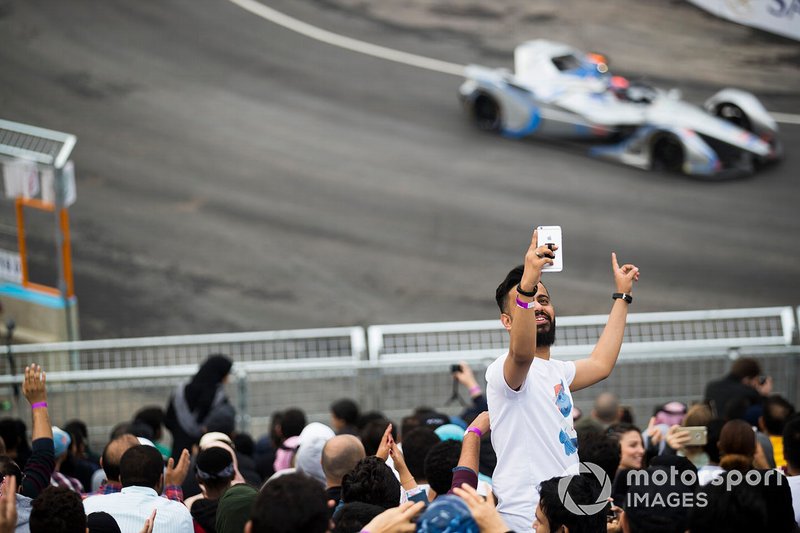 A fan takes a selfie with cars on track behind